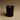 Black candle in a cylindrical container with a visible flame on a beige background